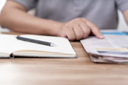 Close up pen on notebook and a man looking newspaper on the wood tableの写真素材