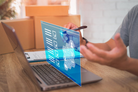 Smart checklist of business work on virtual screen,Close up hand a man holding pen mark on checklist in transport parcel delivery and use laptop working in officeの写真素材