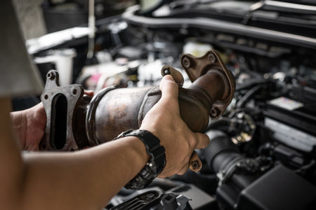 Close up old catalytic converter in hand Car service man remove from engine gasoline car dust clogged condition on filter in service concept and engine room in the backgroundの写真素材