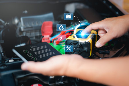 Car service concept,  Employees man push the bottom switch on recharger machine for charger battery of car in engine room and use smartphone check digital checklist in online data service partの写真素材