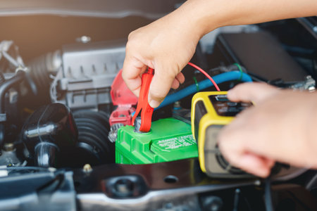 Car service and basic check concept, Technician is using charge charger meter to check battery voltage in engine room and push switch to charger battery and vehicle electrical system basic inspectionの写真素材