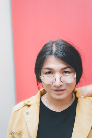 Beautiful asian woman (LGBTQ) natural makeup wear fashion yellow leather clothes with glasses posing at old town and vintage building outdoor fashion styleの写真素材