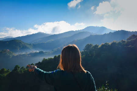 Pretty woman in short jeans with hat hiking in forest on mountain with cliff with happy and freedom emotion in concept travel, active lifestyle, vacation, overcome obstacles in lifeの写真素材