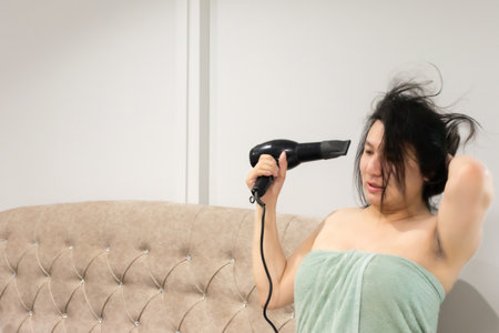 Thai LGBTQ person drying hair after shower relaxing on bed preparing for night routine and content creation in cozy home showing comfort and selfcare lifestyle momentの写真素材