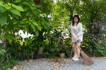 Two LGBTQ friends, one with long hair and the other with short hair, clean and tidy the front yard together in the morning. They sweep fallen leaves and enjoy the peaceful atmosphere in the garden.の写真素材