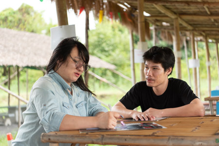 Two LGBTQ friends sitting at an Isaan Thai restaurant, enjoying their lunch together. One is writing...