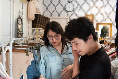 Two LGBTQ friends enjoy shopping for stylish clothes at a boutique. One friend holds a garment while...