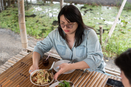 One of the LGBTQ friends is receiving a plate of food at an Isaan Thai restaurant while the other prepares to enjoy the meal. They share a moment of connection and laughter in a cozy, outdoor setting.の写真素材