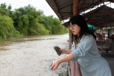 Two LGBTQ close friends feeding fish in the river at a Thai temple alms zone. The scene reflects...