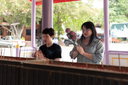 Two LGBTQ friends offering incense and flowers in prayer at a Thai temple. They are performing a spiritual ritual with devotion and respect in a peaceful temple environment.の写真素材