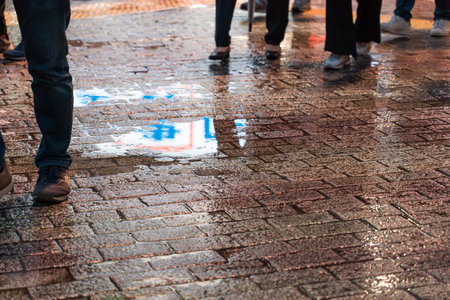 People walking on brick street in rainy evening with sign and lights are reflected in a water puddleのeditorial素材