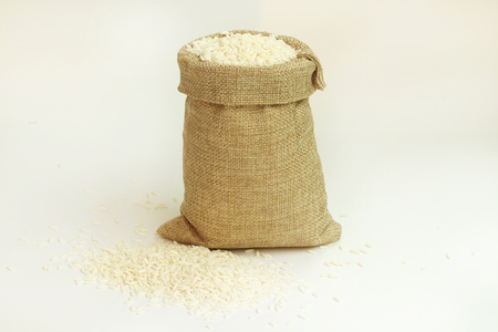 White rice in burlap sack bag on white background.の写真素材