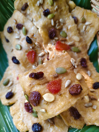 A minimalist still life of elongated banana sticks, air-dried to a soft chew and topped with sunflower seeds, raisins, sesame, and almonds.の写真素材