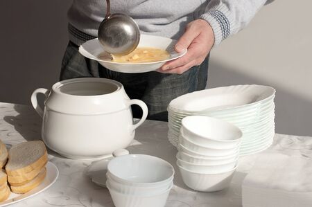 A man pouring chicken soup into white dish from white tureen
