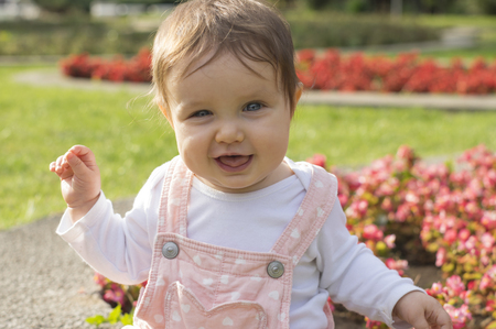 Baby girl in pink is sitting on green meadow and play with flowersの写真素材