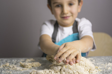 Little boy kneading raw pizza dough. Focus on foreground.