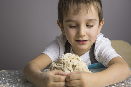 Little boy is kneading raw pizza dough and making a hugの写真素材