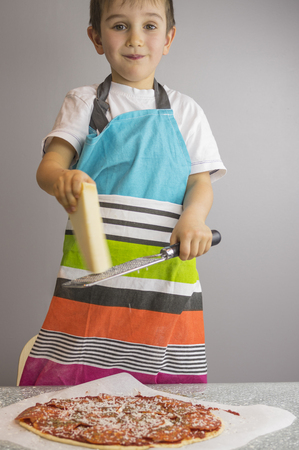 Little boy is making pizza, scrape cheese with graterの写真素材