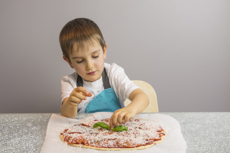 Little boy is making pizza, finishing with basil leafsの写真素材