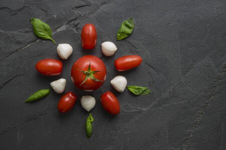 Traditional Italian pizza ingredients mozzarella, salami, tomato and basil leaves composed in a flower shape on black natural stone background. Copyspace. Top view. の写真素材