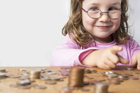 Smiling girl wearing glasses dressed in pink counting coins for savings. Focus on the face. Clean neutral background and copy space on the left.の写真素材