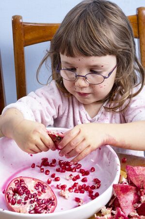 Young girl squeezing pomegranate juice, making a mess on wooden background. Face and clothes dirty with red spots. Autumn healthy concept.の写真素材