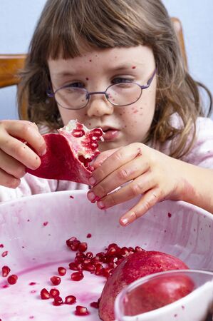 Young girl squeezing pomegranate juice, making a mess on wooden background. Face and clothes dirty with red spots. Autumn healthy concept. Focus on the hands.の写真素材
