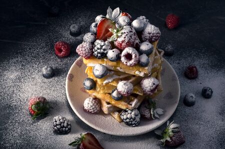 Traditional homemade Belgian waffles with fresh summer berries, blueberry raspberry, strawberry and blackberry dusted with icing sugar. Delicious breakfast. Selective focus.の写真素材