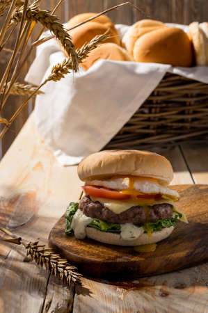 Street food, fast pub food. Homemade juicy burgers with beef, cheese tomato, salad and egg onions on  wooden table. Sharp light for summer harvest mood.の写真素材