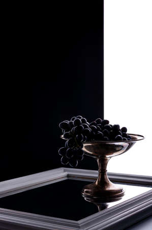 A goblet of black grape stands on a mirror on split black and white background. Minimal compositionの写真素材