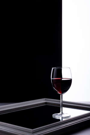 A glass of wine stands on a mirror on split black and white background. Minimal compositionの写真素材