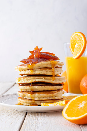 Pancake tower with orange marmalade, fresh oranges and juice for breakfast on rustic wooden table