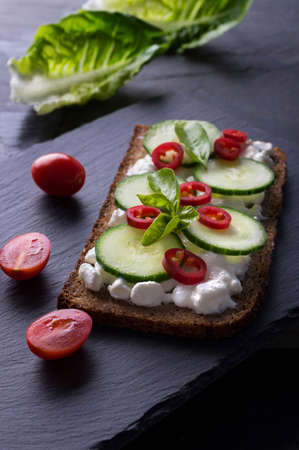Fresh spring sandwich on a sliced gluten free sunflower bread. Red and green vegetables on black...