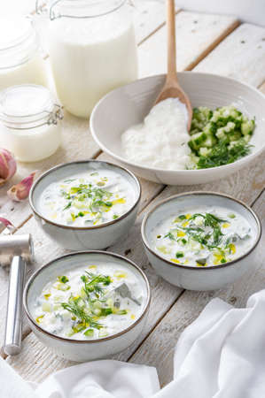 Traditional summer cold soup of homemade yogurt, cucumbers and fresh herbs on a wooden tableの写真素材