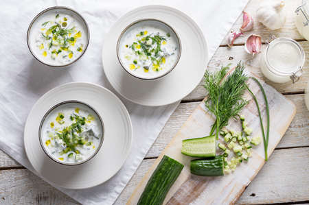 Traditional summer cold soup of homemade yogurt, cucumbers and fresh herbs on a wooden tableの写真素材