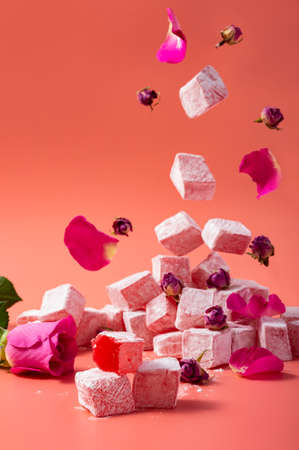 Levitating rose flavored pink Turkish delight with flower petals and dry rose buds on pink backgroundの写真素材