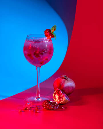 Gin and tonic pomegranate cocktail with ice cubes and mint leaves on abstract red and blue background. Neutral copy spaceの写真素材