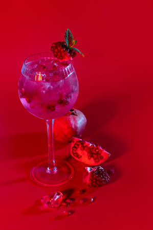 Gin and tonic pomegranate cocktail with ice cubes and mint leaves on abstract red background. Neutral copy spaceの写真素材