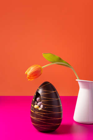 Easter chocolate egg with spring tulips on vibrant orange background