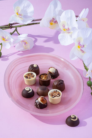 Handmade rustic chocolate truffles with white orchid flowers on pink background