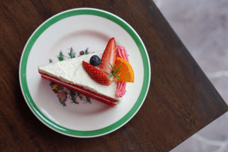 top view strawberry and orange and blueberry on white and red cake, on white and green ceramic...
