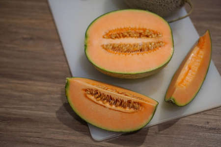closeup two cantaloupe on a white plastic chopping board on wooden floor backgroundの写真素材