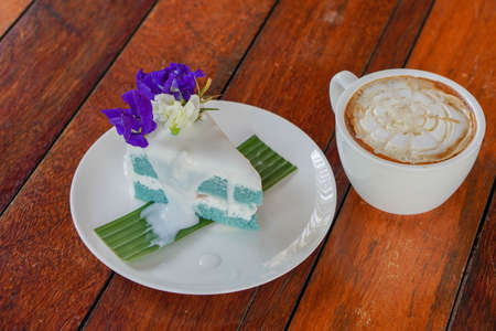 top view Coconut Cake on green banana leaf on white ceramic plate and coffee in white ceramic mug, on wooden floor background, food, dessert, copy spaceの写真素材