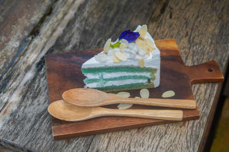 cake with three layer of cake and three layer of white cream, on top by coconut and a butterflypea flower, sprinkle with almond slices which place on brown chopping board and two light brown wooden spoons, on wooden table backgroundの写真素材