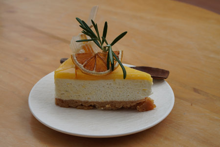 honey slice, dry orange slice, green leaf, wooden spoon, on yuzu cheese pie on white ceramic plate...
