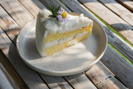closeup side view cake decorated with yellow pollen and violet flowers and green leaves on a ceramic plate on bamboo table background, food, dessert, copy spaceの写真素材