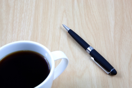Cup of coffee on a wooden table with penの写真素材
