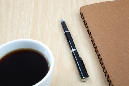 Cup of coffee on a wooden table with book and penの写真素材