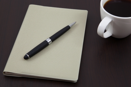 Cup of coffee on a wooden table with book and penの写真素材