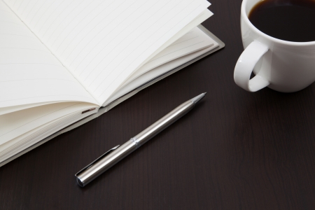 Cup of coffee on a wooden table with book and penの写真素材